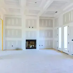 Interno di una casa in costruzione con pareti e soffitti rifiniti con rivestimento in cartongesso, camino e porte a doppio battente.