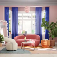 Ein rosa Sofa wird von kräftigen blauen Vorhängen und einem bunten Teppich umrahmt. Welche Farbe passt zu rosa? Hier: Blau, Orange und Grün!