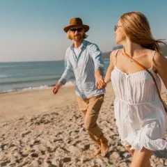 Szczęśliwa para biegnie plażą, trzymając się za ręce. Słońce, morze i piaszczysta promenada nad morzem tworzą idealne tło dla ich wakacyjnej przygody.