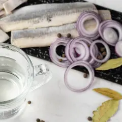 Förberedelser för inlagd sill: sillfiléer, rödlök, lagerblad, pepparkorn och en bägare med ättika. 1, 2, 3 lag.