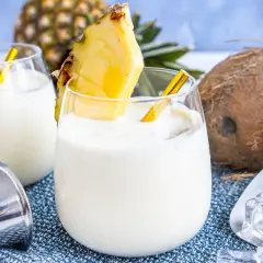 Zwei cremige Kokos-Ananas-Cocktails, garniert mit Ananasstücken, versprechen einen tropischen Genuss. Ein Hauch von "coconut kiss" für heiße Tage.
