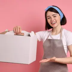 Uśmiechnięta cukierniczka pokazuje, jak złożyć pudełko na tort. Gotowa do zapakowania pyszności!