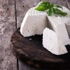 Ricotta fatta in casa, fresca e profumata, guarnita con basilico, pronta per essere gustata su un tagliere di legno rustico.