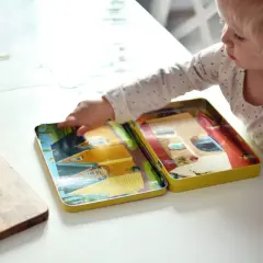 Małe dziecko bawi się otwartym pudełkiem z obrazkami domków, które są świetnymi zabawkami wspierającymi rozwój mowy.