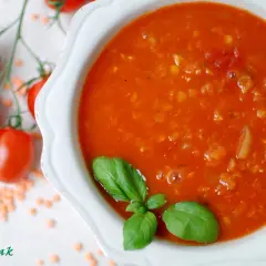 Zupa pomidorowa z soczewicą, ozdobiona bazylią. Obok gałązka pomidorków i rozsypana soczewica. Idealna na chłodne dni, smakuje jak domowe pesto pomidorowe.