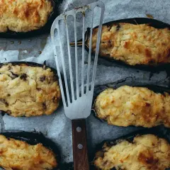 Halverade auberginer fyllda med en krämig blandning, gyllene och gratinerade i ugn. En spatel ligger bredvid, redo att servera.