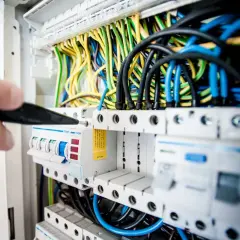 Ręka z narzędziem przy bezpiecznikach. Dowiedz się, jak sprawdzić bezpiecznik automatyczny w skrzynce z przewodami.