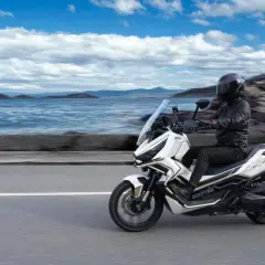 Conductor en moto Zontes 368G blanca, con paisaje marino y montañas. ¡Las opiniones sobre esta moto son excelentes!