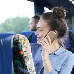 Kobieta w autobusie rozmawia przez telefon, zastanawiając się, jak włączyć roaming w Plus.