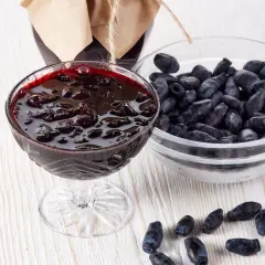 Pyszny dżem z jagody kamczackiej w kielichu, obok miseczka świeżych owoców i słoik przetworów.