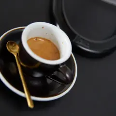 Aromatyczne włoskie espresso w filiżance z złotą łyżeczką na czarnym tle. Idealny początek dnia.