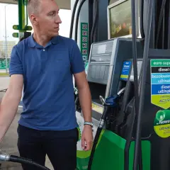 Mężczyzna tankuje samochód, pokazując, jak zatankować auto. Widoczna jest dystrybutor paliwa z różnymi rodzajami paliwa.