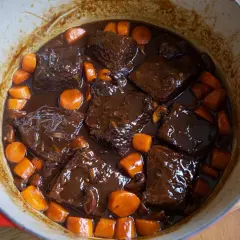 Sabroso plato típico de Francia: ternera estofada en salsa oscura con zanahorias y champiñones en una olla roja.