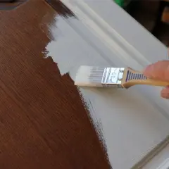 Une main applique une sous-couche claire sur un meuble en merisier, avant de le repeindre en noir.