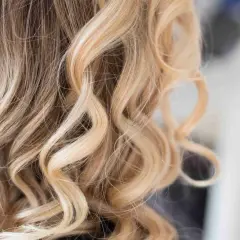 Falowane blond włosy z jaśniejszymi pasemkami, tworzące naturalne rozświetlenie.
