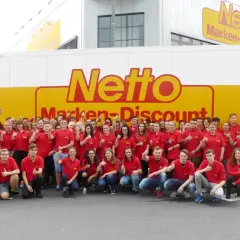 Gruppe von Mitarbeitern in roten T-Shirts vor einem Netto-LKW. Eine gute e-commerce ausbildung gehaltsperspektive für die Zukunft.