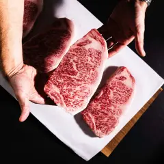 Des mains présentent des steaks de bœuf persillés, marbrés de gras, promettant le meilleur bœuf du monde.