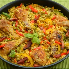 Aromatyczna paella z kurczakiem, ryżem, groszkiem i kolorową papryką, podana w czarnej patelni na zielonej macie.
