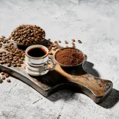 Chicco di caffè, macinato e bevanda scura su tagliere rustico. Chi dice che il caffè fa male, non ha visto questa meraviglia.