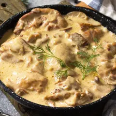 Kurczak w kremowym sosie z grzybami i koperkiem w czarnej patelni.
