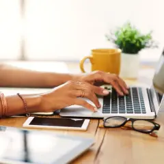 Kobieta pracuje na laptopie, planując swój mały ZUS na ryczałcie. Na biurku leżą też tablet, telefon i okulary.