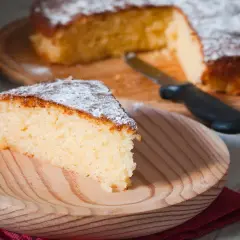 Una fetta di torta all'acqua soffice e spolverata di zucchero a velo su un piatto di legno.