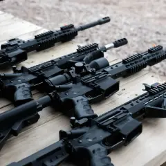 Kilka karabinów AR15 leży na drewnianym stole. W tle widać pudełko z amunicją.