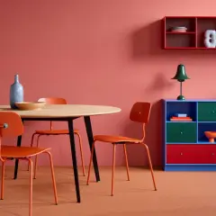 Ein Essbereich mit orangefarbenen Stühlen und einem Holztisch vor einer korallenroten Wand. Die Wandfarbe erinnert daran, wie man dunkelrot mischt.