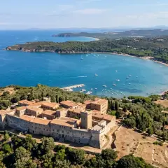 Fortezza del Poggio, una delle meraviglie del Val di Cornia cosa vedere, domina una baia azzurra con barche e una spiaggia dorata.