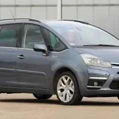 Szary Citroen C4 Grand Picasso 2.0 HDI z kierowcą za kierownicą, zaparkowany przed budynkiem.