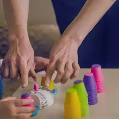 Dziecko i dorosły ćwiczą z kolorowymi kubeczkami i klepsydrą.