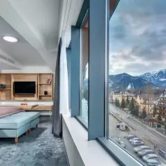 Pokój w hotelu Novotel z widokiem na góry. Wygodne łóżko, telewizor i przestronne okno z panoramą miasta i ośnieżonych szczytów.