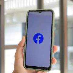 Dłoń trzyma smartfon z logo Facebooka. Chcesz wiedzieć, jak wyłączyć urodziny na FB?