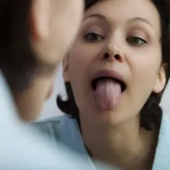 Donna si guarda allo specchio, mostrando la lingua. La saliva aiuta a digerire e a mantenere la bocca sana.