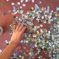 Ręka układa puzzle do układania na drewnianym stole obok kubka kawy.