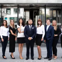 Grupa profesjonalistów w eleganckich strojach stoi przed nowoczesnym budynkiem.