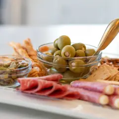 Plateau apéro raclette : olives, pistaches, salami, bretzels et crackers. Parfait pour un moment convivial.