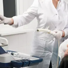Arzt führt eine Untersuchung mit einem Ultraschallgerät durch. Die Patientin liegt auf dem Tisch.
