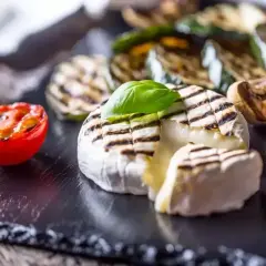 Ciepły camembert z grilla, z roztopionym wnętrzem, podany z grillowanymi warzywami i pomidorkiem.