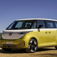 Minivan elettrico Volkswagen ID. Buzz bicolore giallo e bianco, parcheggiato su un terreno sterrato con sfondo di colline e cielo azzurro.