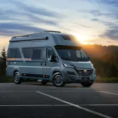 Nowe kampery Globe Traveller zapraszają na przygodę. Szary Fiat Ducato z nowoczesnym designem na tle zachodzącego słońca i lasu.