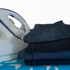 Fer à repasser et pile de vêtements sombres sur une planche à repasser. Apprenez comment repasser du polyester pour un résultat impeccable.