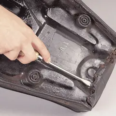 Mano usa cacciavite per rimuovere rivestimento sella moto, parte di un kit riparazione sella moto.