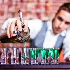 Barman nalewa zielony shot do kieliszków. Zastanawiasz się, ile zarabia barman na godzinę?