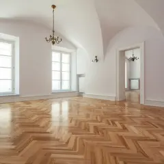 Un ampio salone con parquet a spina di pesce appena levigato, illuminato da grandi finestre e lampadari antichi.