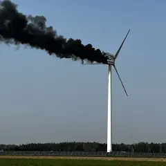 Płonąca turbina wiatrowa z gęstym, czarnym dymem unoszącym się na tle błękitnego nieba.