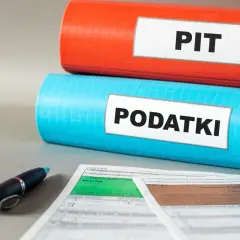 Dwa segregatory z napisami "PIT" i "PODATKI", obok formularze podatkowe i długopis. Kto nie płaci podatku do 26 roku życia?