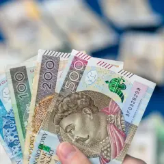 Dłoń trzyma wachlarz polskich banknotów: 50, 100, 200 i 500 zł. To dowód, że można być aktywnie w domu dla każdego, kto oszczędza.