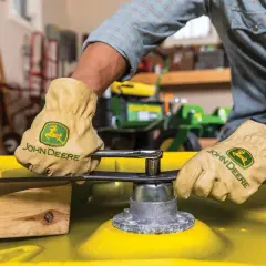 Gloves on, a person uses a socket wrench to remove a mower blade, preparing to sharpen it.