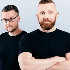 Dwóch mężczyzn w czarnych koszulkach, jeden w okularach, drugi ze skrzyżowanymi rękami. Wyglądają jak duet Catz n Dogz.